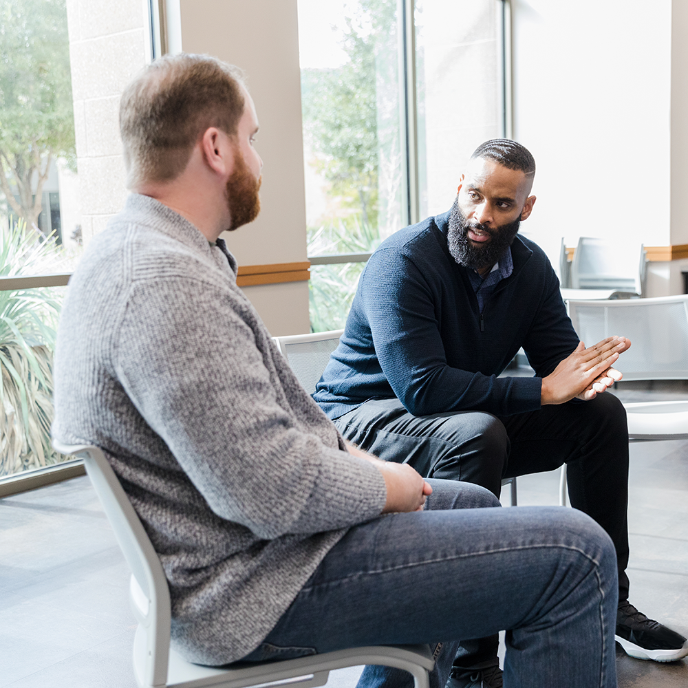 A photo of two men talking to one another in a therapy style situation.