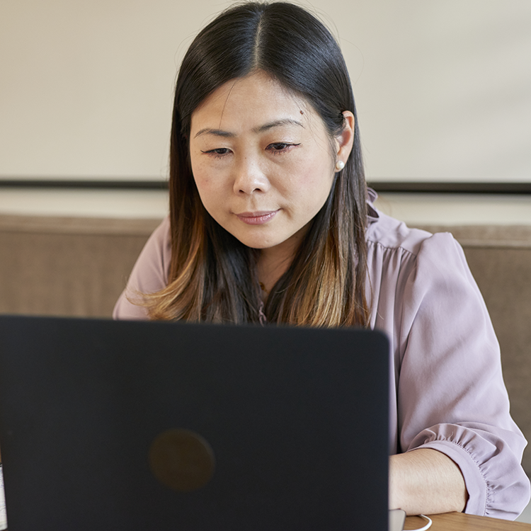 A photo of an asian woman using a computer to look through an online library.